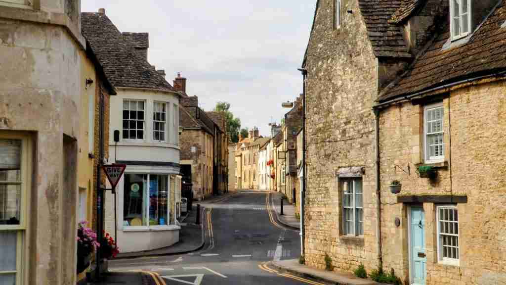 Minchinhampton’s narrow street with Cotswold stone cottages. Narrow street in Minchinhampton lined with 17th‑ and 18th‑century Cotswold stone cottages and small shops, reflecting the town’s historic market‑town character
