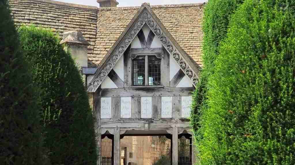 Half‑timbered lych gate at St Mary’s churchyard, Painswick, built in 1901 from old belfry timber Half‑timbered lych gate at St Mary’s churchyard in Painswick, built in 1901 using old belfry timbers with cross‑gabled roof and bench seat
