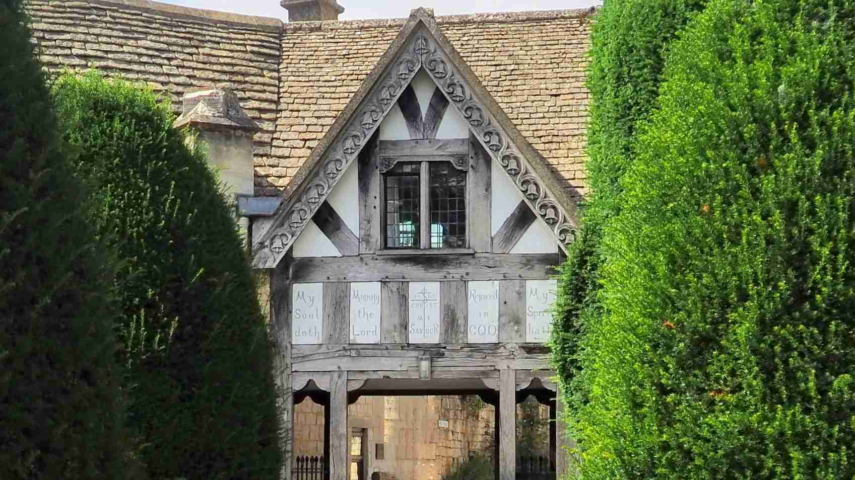 Half‑timbered lych gate at St Mary’s churchyard, Painswick, built in 1901 from old belfry timber Half‑timbered lych gate at St Mary’s churchyard in Painswick, built in 1901 using old belfry timbers with cross‑gabled roof and bench seat